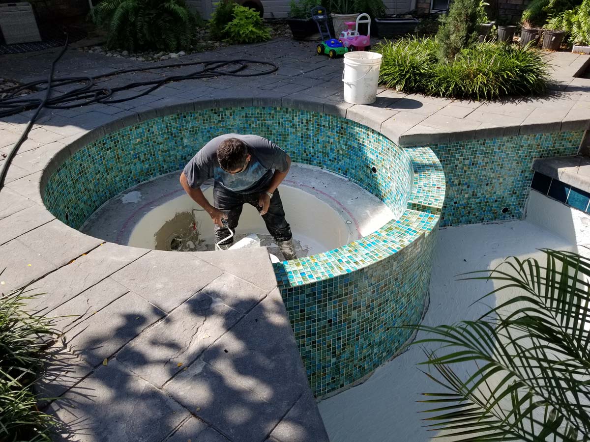 20180821_111606 Photo showing a pool and hot tub that have been drained of water for cleaning and remodeling work. Pool surface is a light blue color and tiles around the pool and hot tub are a mixture of blue and green colors.