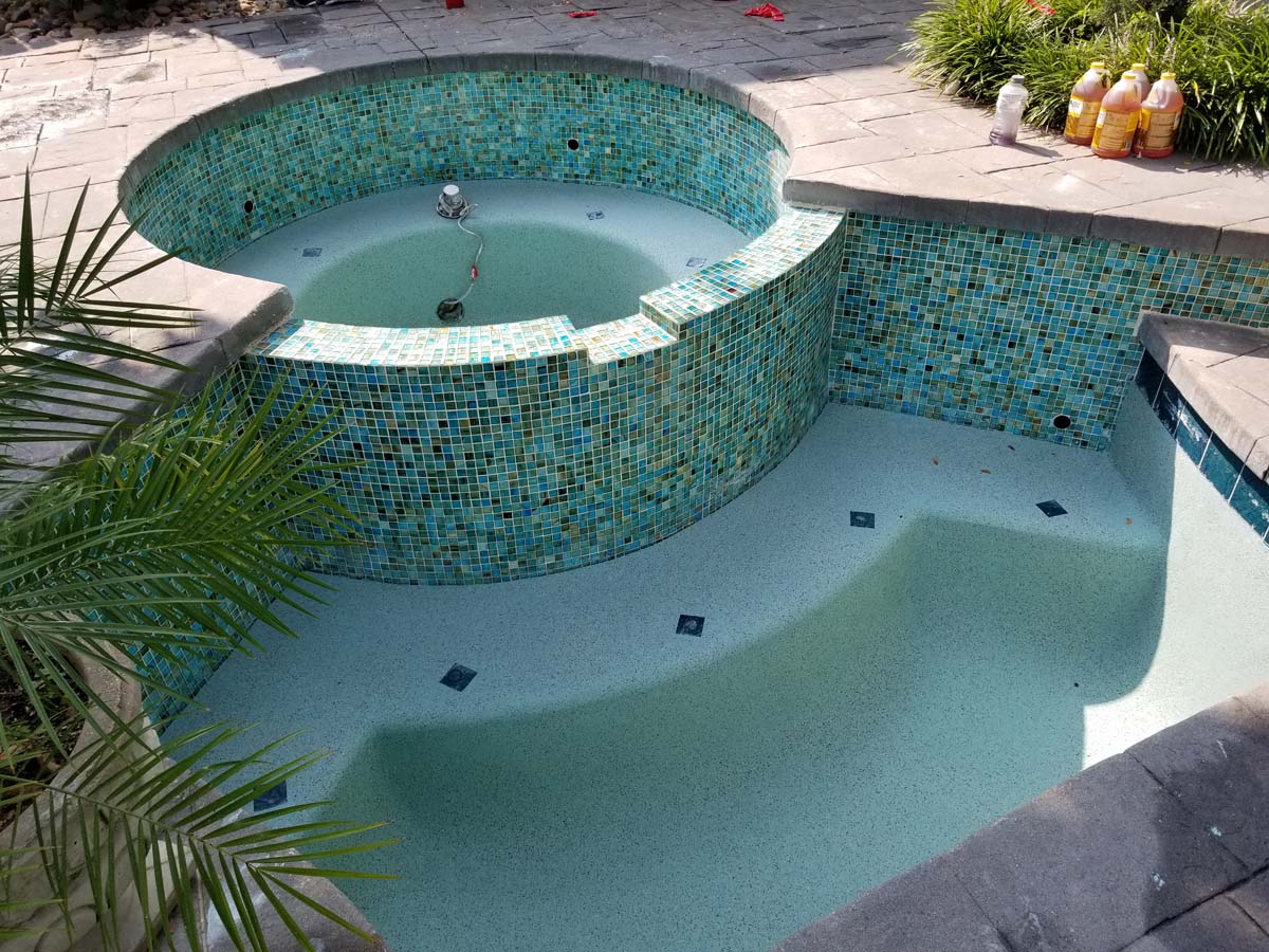 20180821_104157 Another picture showing a pool and hot tub that have been drained of water for cleaning and remodeling work. A different view shows the pool surface is a light blue color and tiles around the pool and hot tub are a mixture of blue and green colors.