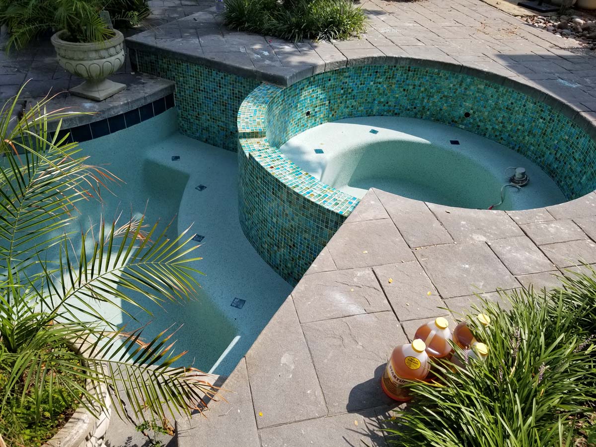 20180821_111606 Photo showing a pool and hot tub that have been drained of water for cleaning and remodeling work. Pool surface is a light blue color and tiles around the pool and hot tub are a mixture of blue and green colors.