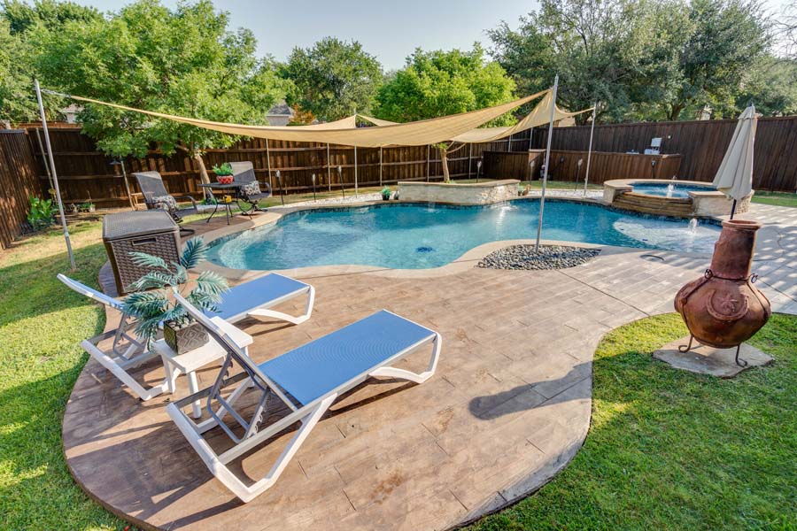 Weekly Pool Cleaning Service by Flower Mound Pool Care and Maintenance. Image of a jacuzzi in the background taken from an angle in back of house. Image shows sun shade over the pool.