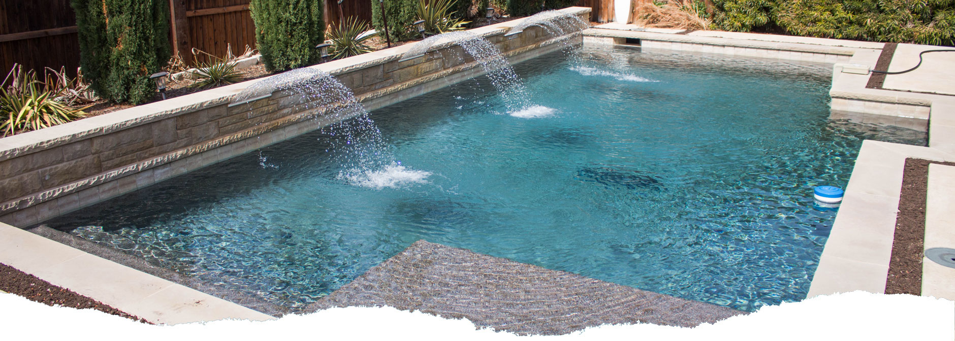 Picture of a rectangular pool with blue water and three water fall features shooting water into the pool.