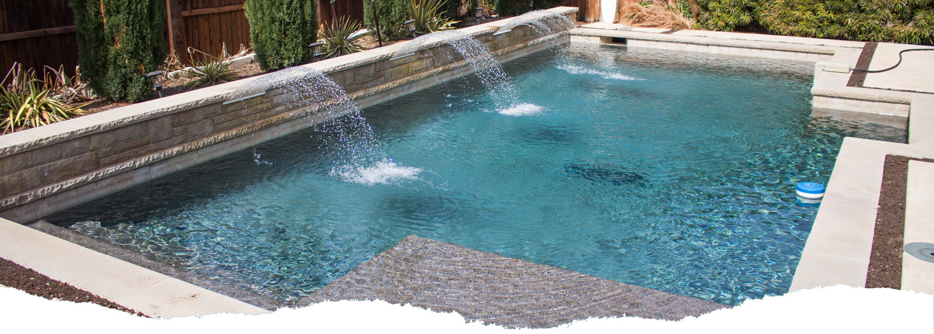 Picture of a rectangular pool with blue water and three water fall features shooting water into the pool. Picture of a rectangular pool with blue water and three water fall features shooting water into the pool.