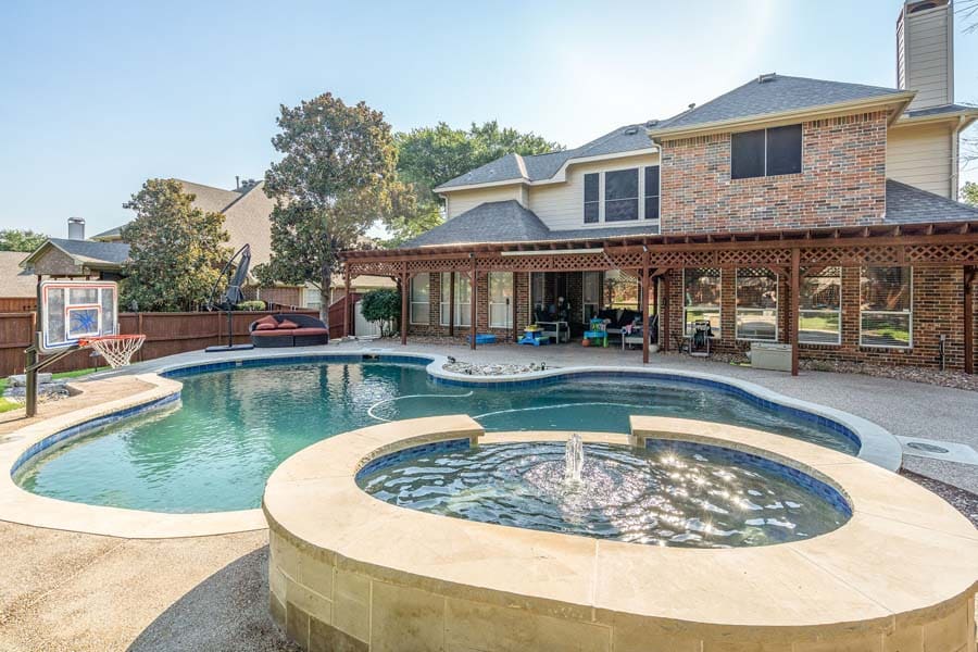 Weekly Pool Cleaning Service by Flower Mound Pool Care and Maintenance. Image of pool and jacuzzi in the foreground taken from a side angle in back of house.