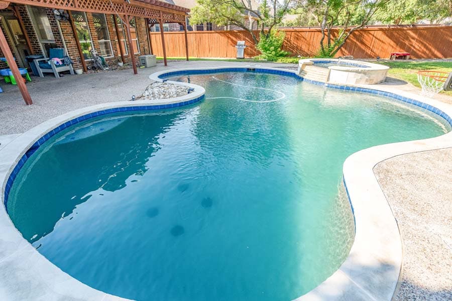 Weekly Pool Cleaning Service by Flower Mound Pool Care. Image of pool and jacuzzi in the back.