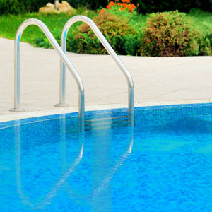 Picture of pool with pool ladder, shrubs in the back ground and blue pool water.