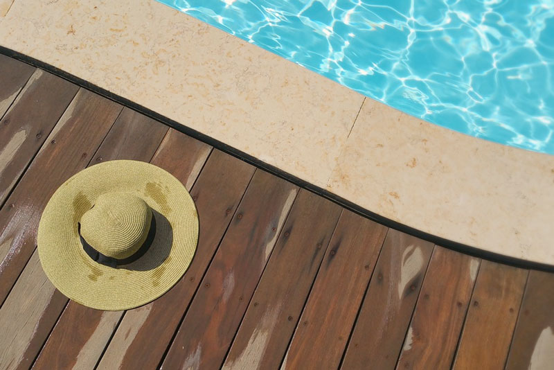 Photo of the side of pool area with a wood deck and a sun hat laying on the wood deck.