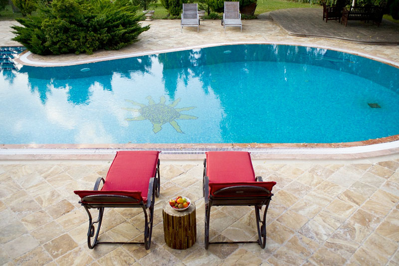 Photo of a backyard pool with blue waters, a sun shaped pool feature on the bottom of the pool. Several lounge chairs are shown around the pool.